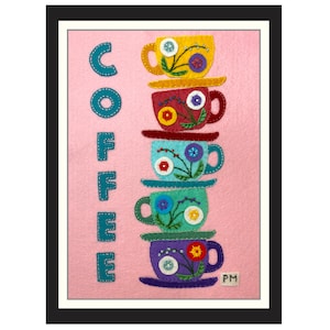 May include: A pink felt background with the word "COFFEE" in teal stitched letters. A stack of five colorful felt coffee cups with floral designs and white buttons are stacked on top of each other. The bottom cup has a saucer and the text "PM" in white.