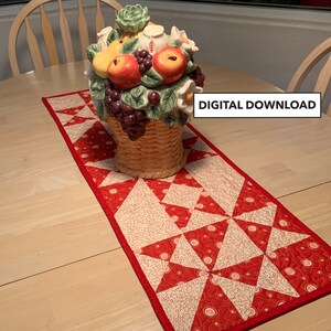 May include: Red and white quilted table runner with a geometric pattern. The runner is on a wooden table with a ceramic fruit basket in the centre.