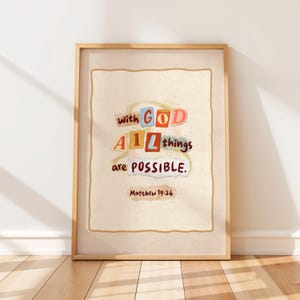 Op de afbeelding: Een ingelijste print met de tekst "With God All things are Possible" in kleurrijke blokletters. De tekst staat tegen een crèmekleurige achtergrond met een gescheurd papiereffect, en de lijst is lichtbruin.