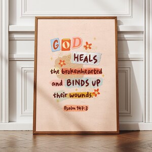 May include: A framed print featuring the text "GOD HEALS the brokenhearted and BINDS UP their wounds." The words are in different colours and fonts, with floral decorations. The bottom of the print reads "Psalm 147:3". The frame is a warm brown.