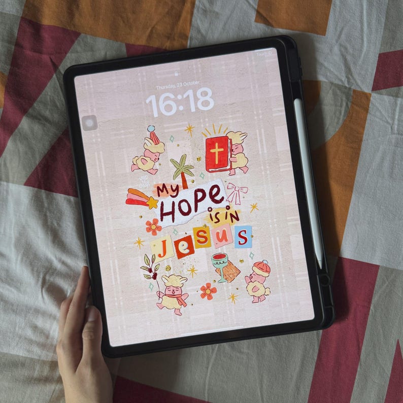Op de afbeelding: Een zwarte tablet met een scherm met de woorden "My Hope is in Jesus" in kleurrijke letters en illustraties. Het scherm toont ook de tijd en datum. Een witte stylus is aan de zijkant bevestigd.