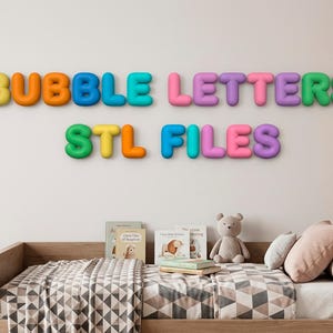 May include: A wall display featuring multi-colored, three-dimensional bubble-style letters that spell out BUBBLE LETTERS STL FILES. The letters are arranged in two rows against a plain wall above a wooden bed frame with pillows and books.