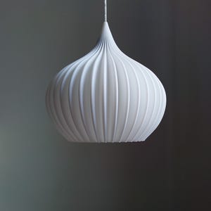May include: White pendant light fixture with a ribbed, onion-shaped design. The light hangs from a thin white cord against a neutral gray background. The fixture has a smooth, matte finish and a teardrop shape.