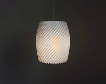 May include: A white, cylindrical pendant light with a spiral design. The light fixture is suspended from a thin wire and has a textured surface. The light is turned on, emitting a soft glow.
