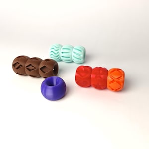 May include: A collection of colorful, 3D-printed beads in various shapes and designs. The beads are in shades of brown, teal, red, orange, and purple. Some beads have geometric patterns, while others have heart and wave designs. The beads are displayed on a white surface.