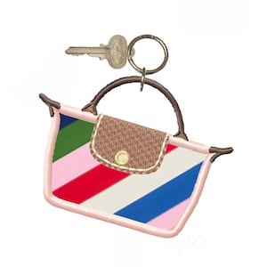 May include: A colorful handbag keychain with a key and a key ring. The handbag is embroidered with diagonal stripes in green, pink, red, white, and blue. The flap is brown with a gold button. The handle is brown.