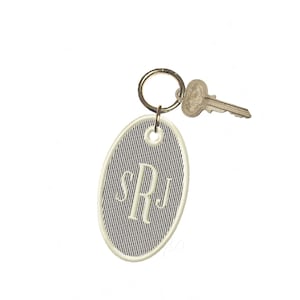 Puede incluir: Llavero ovalado con un diseño de rayas azul marino y blanco, con las iniciales "SRJ" bordadas en una fuente serif. Una llave y un llavero plateados están unidos, creando un accesorio personalizado.