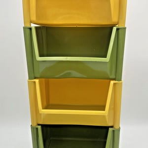 May include: A four-tier vertical storage unit featuring alternating yellow and olive green plastic bins. The structure consists of stackable open-front containers supported by integrated vertical posts, creating a modular shelving system for organisation.