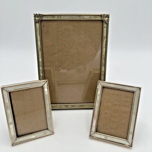 以下が含まれることがあります： 3つのアンティークフォトフレーム。最大のフレームは、装飾的なコーナーディテールを備えた長方形です。2つの小さなフレームも長方形で、真珠母貝のボーダーが付いています。すべてのフレームには茶色の裏地が付いています。