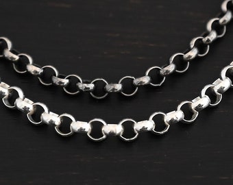 May include: Two silver chains, one thicker than the other, lay on a dark wooden surface. The chains are made of small, round links.
