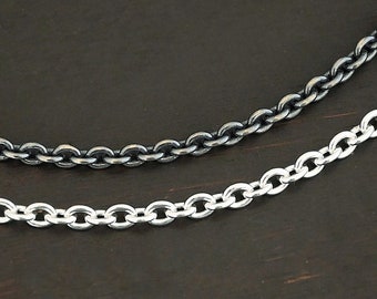 May include: Two silver chains, one oxidized and one polished, lay side-by-side on a dark wood surface.
