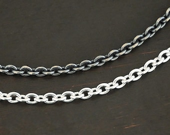 May include: Two silver chains, one oxidized and one polished, lay on a dark brown wooden surface.