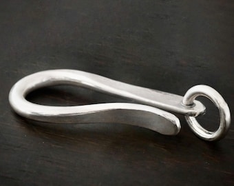 May include: A silver key chain with a hook and a ring. The hook is curved and the ring is round. The key chain is on a dark wooden surface.