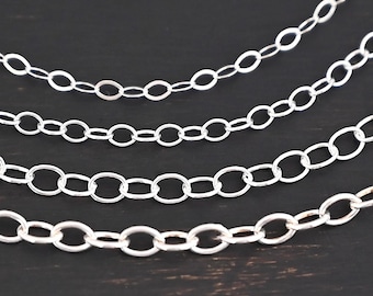 May include: Five silver chains of different lengths and thicknesses, arranged in a graduated pattern on a dark wooden surface.
