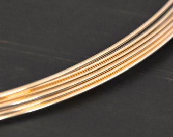 Può includere: Primo piano di un fascio di sei fili metallici dorati. I fili sono disposti a semicerchio e giacciono su una superficie scura.