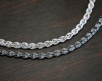 May include: Two silver chains with a rope design, one is silver and the other is black, both are on a dark brown wooden surface.