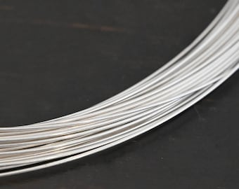 Puede incluir: Primer plano de un haz de alambre de plata. El alambre está enrollado y dispuesto en una pila ordenada.