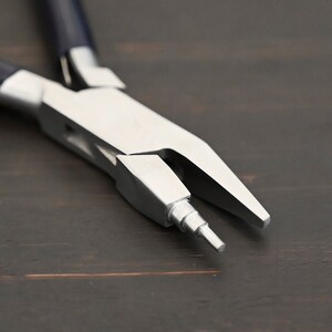 May include: Close-up of a pair of silver-toned pliers with blue handles. The pliers have a pointed tip and a small, round knob on the side.