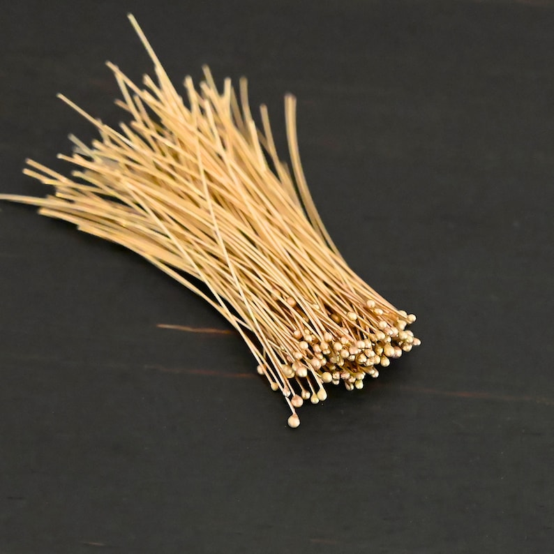 May include: A bunch of gold-colored floral wire with small round heads. The wire is arranged in a loose bundle, with the heads at the bottom.