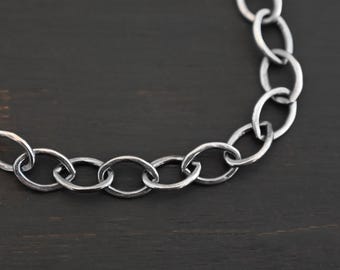May include: A silver chain necklace with oval links. The chain is on a dark wood background.