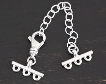 May include: Silver extender chain with a lobster clasp on one end and a T-bar with three loops on the other end.