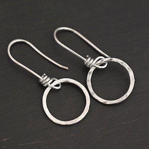 May include: A pair of silver hoop earrings with a hammered finish. The hoops are attached to a silver wire that is twisted at the top.