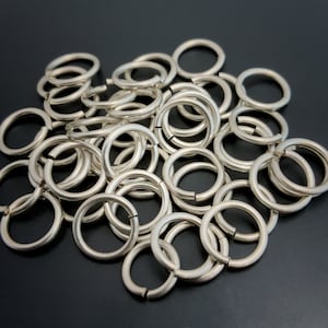 May include: A pile of silver jump rings, a type of metal ring used in jewelry making.