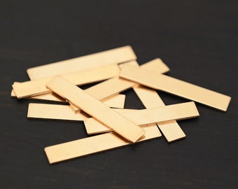 May include: A pile of thin, rectangular brass sheets, stacked and overlapping on a dark surface.