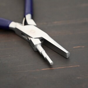 May include: Close-up of a silver jewelry pliers with blue handles. The pliers are open and the jaws are extended.