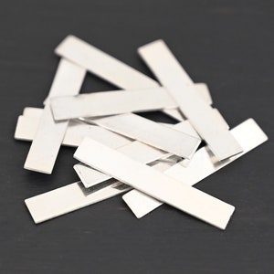 Op de afbeelding: Een stapel van tien zilveren rechthoekige metalen blanco's. De blanco's zijn glad en glanzend.