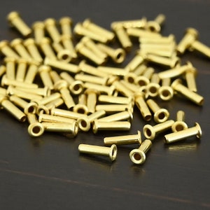 May include: A large pile of gold-colored metal eyelets. The eyelets are small, cylindrical tubes with a hole at one end. They are used for attaching fabric or other materials to a surface.