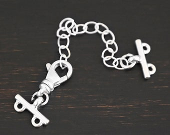 May include: Silver chain with a lobster clasp and two toggle clasps. The chain is made of small, round links.
