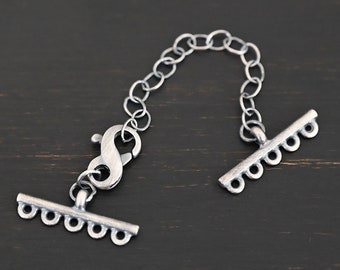 May include: Silver toggle clasp with a chain connector. The clasp has five loops on each side and a silver lobster claw clasp.