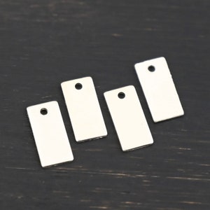 May include: Four silver rectangular metal tags with a hole at the top. The tags are blank and have a shiny finish.