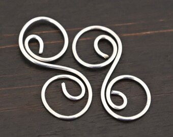Könnte beinhalten: Silberner Metalldraht, zu einem dreifachen Schleifendesign verdreht, das einem stilisierten Kleeblatt ähnelt.