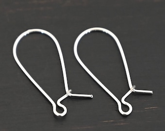 May include: Two silver earring hooks, also known as French hooks, are shown on a dark wood surface. The hooks are made of metal and have a smooth, polished finish.
