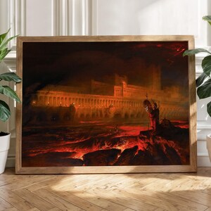 Könnte beinhalten: Ein gerahmter Druck eines dramatischen, feurigen Landschaftsgemäldes. Das Kunstwerk zeigt eine große, beleuchtete Struktur mit Figuren, vor einem dunklen, bedrohlichen Himmel und einem roten, lavaartigen Vordergrund. Der Rahmen ist aus Holz.