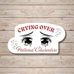 Puede incluir: Una pegatina blanca con el texto "Crying Over Fictional Characters" en rojo y negro. La pegatina presenta una ilustración de dibujos animados de ojos grandes y expresivos con lágrimas y corazones.