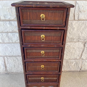 May include: A tall, narrow chest of drawers constructed from dark brown bamboo-style wood. The unit features five horizontal drawers, each with a textured, slatted front panel and a circular brass pull handle centered on the face of every drawer.