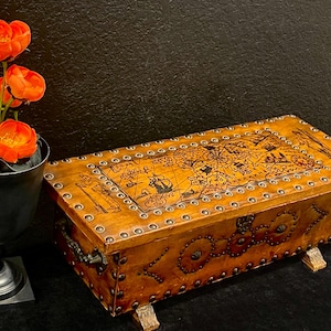 May include: A rectangular wooden chest with a light brown finish, featuring a decorative map print on the lid, metal stud accents along the edges, and small wooden feet. The chest has a dark metal handle on the side and a vintage-style design.