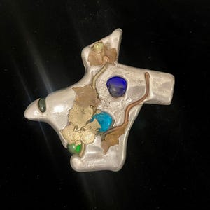 Escultura única de mapa de Texas firmada por Lee Benner. Combinación de metal, latón, cobre, peltre, acero inoxidable, vidrio fundido y forro de terciopelo. 13,7 cm.