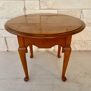 May include: A small, round wooden side table with a glossy finish. The table has a dark brown stain, a scalloped apron, and curved legs. The table is approximately 24 inches in diameter and 20 inches tall.