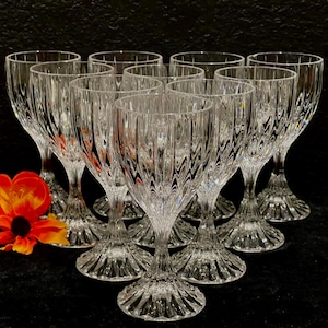 May include: A set of clear crystal wine glasses with a textured, vertical pattern. The glasses are arranged in a group, showcasing their elegant design. An orange and yellow flower is in the foreground.