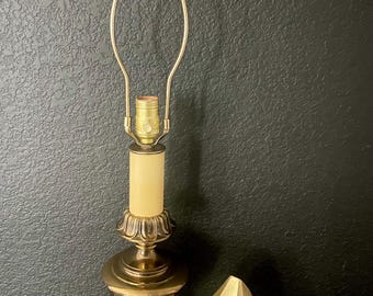 May include: A vintage brass table lamp with a decorative finial and a cream-colored shade. A gold-colored geometric sculpture sits beside the lamp. The lamp has a classic design, suitable for home decor.