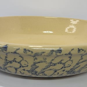 May include: A ceramic serving bowl with a cream-colored interior and a blue and cream patterned exterior. The bowl has a rounded shape and a slightly raised rim. The design is reminiscent of vintage stoneware.