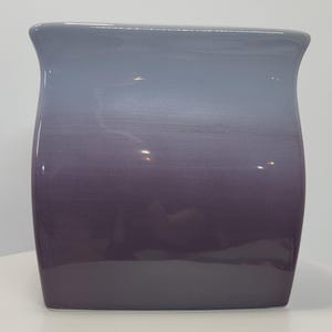 May include: A square ceramic vase with a smooth, glossy finish featuring a vertical color gradient that transitions from a light grey at the top rim to a deep, dark purple at the base. The vessel has slightly curved sides and a wide opening.