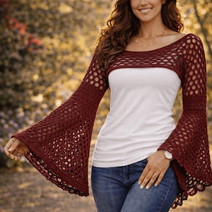 May include: A burgundy crochet shrug with bell sleeves is worn over a white top and blue jeans. The crochet pattern is open, creating a delicate, airy look. The image includes the text "Crochet Pattern - XS to 5XL".