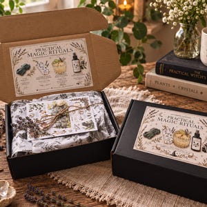 May include: Two black cardboard boxes labelled Practical Magic Rituals, one open and one closed. The open box contains white tissue paper with botanical prints, a card tied with twine, and a lid featuring illustrations of ritual items.