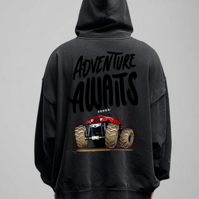 Peut inclure: Sweat-shirt &agrave; capuche noir avec l'inscription "Adventure Awaits" et un dessin de monster truck rouge. Le camion a de gros pneus et un ch&acirc;ssis bleu. Le sweat-shirt a un aspect vintage d&eacute;lav&eacute;.