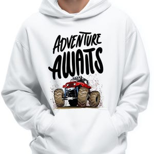 Peut inclure: Sweat &agrave; capuche blanc avec un motif de monster truck rouge et les mots "ADVENTURE AWAITS" en noir. Le design comprend des &eacute;claboussures de boue marron, cr&eacute;ant un th&egrave;me dynamique et aventureux.